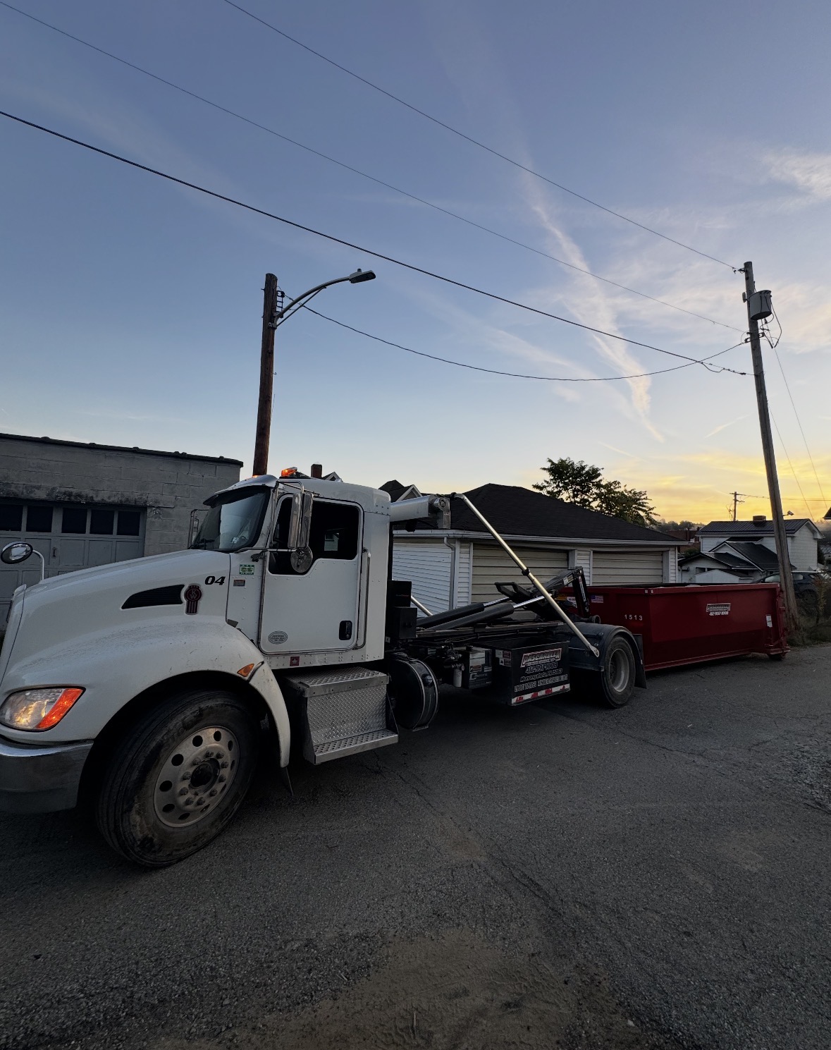 Pascarella truck dropping a roll-off dumpster at sunset in a Pittsburgh neighborhood