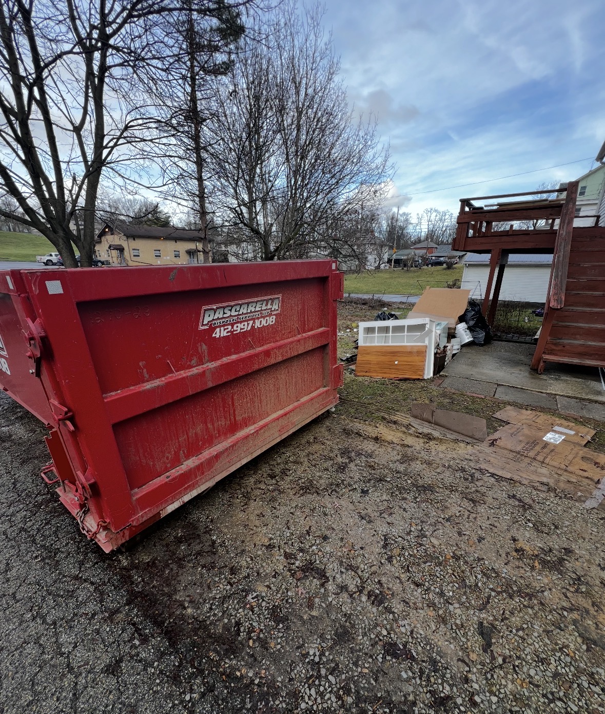 Rear view of a Pascarella dumpster placed beside outdoor cleanup debris in a backyard