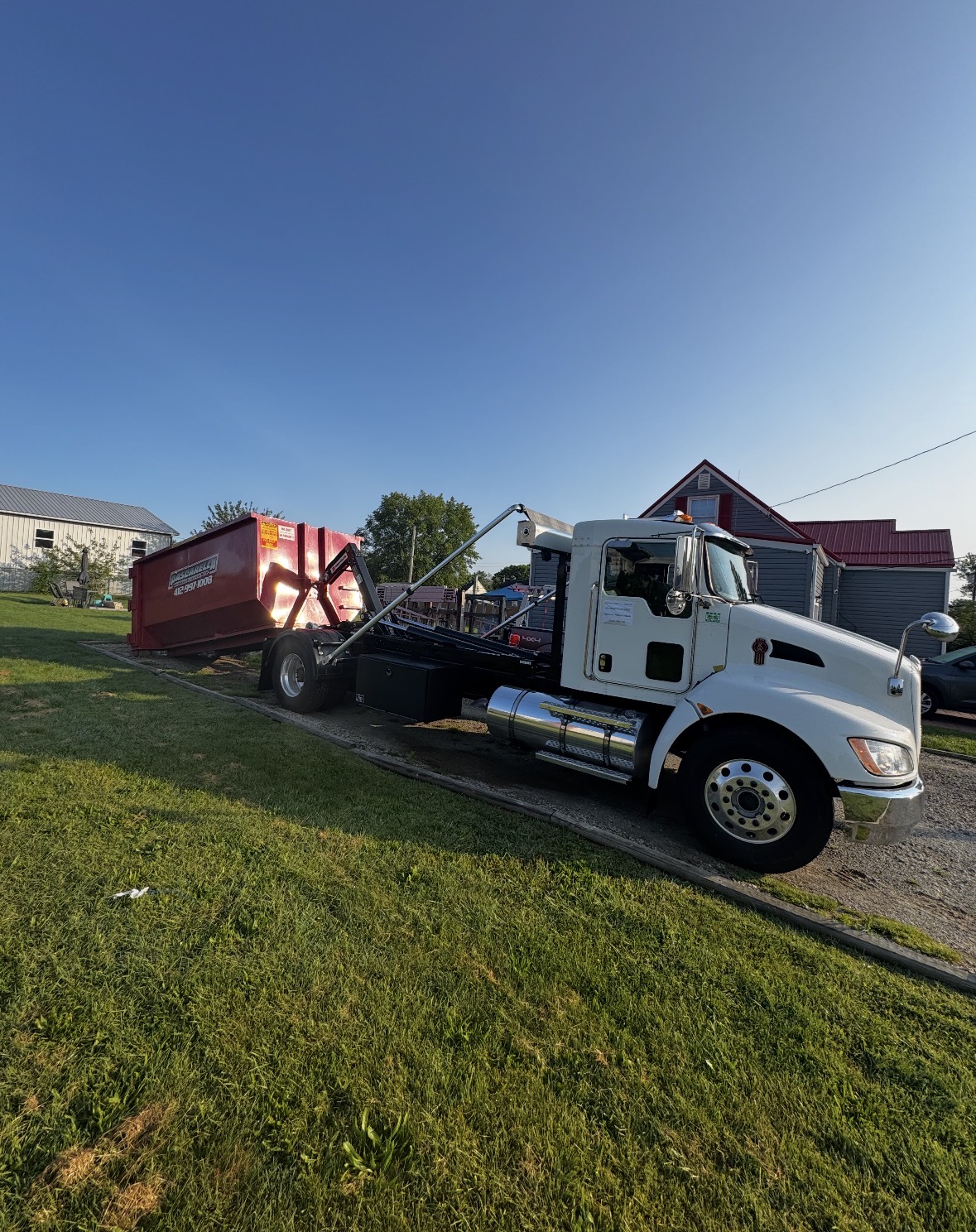 Pascarella roll-off truck loading a red dumpster on a sunny rural property