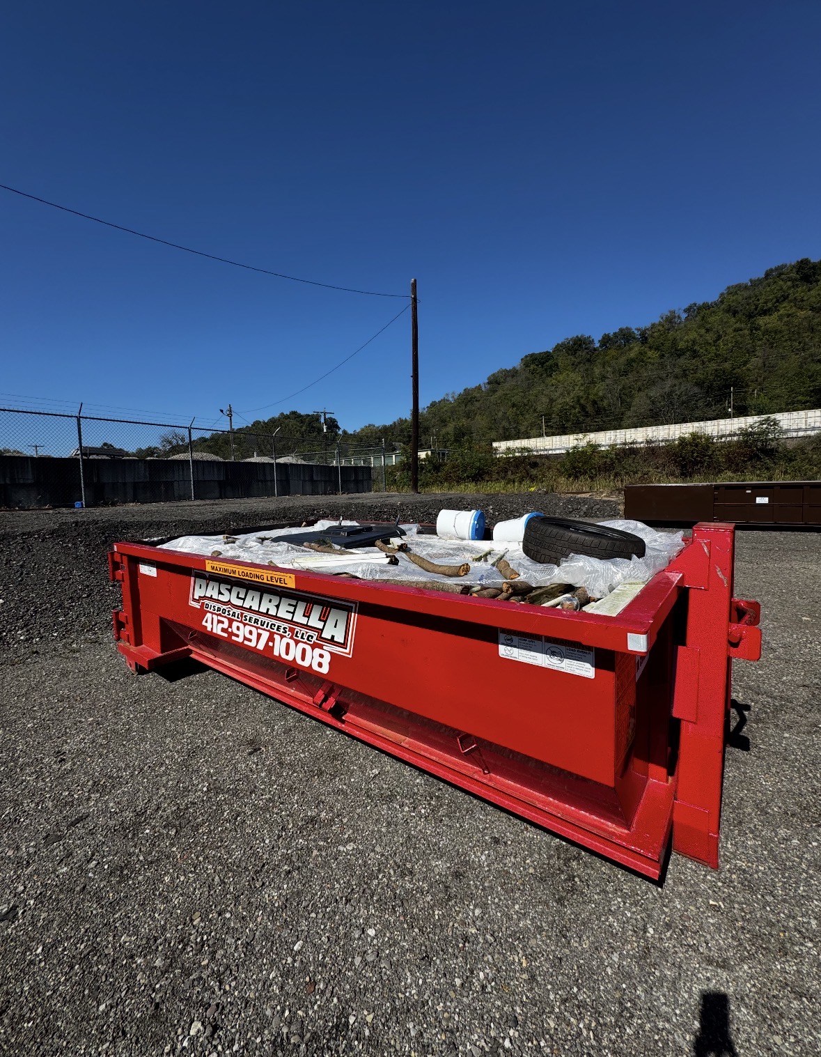 Loaded Pascarella dumpster with debris under a clear blue sky in the Mon Valley
