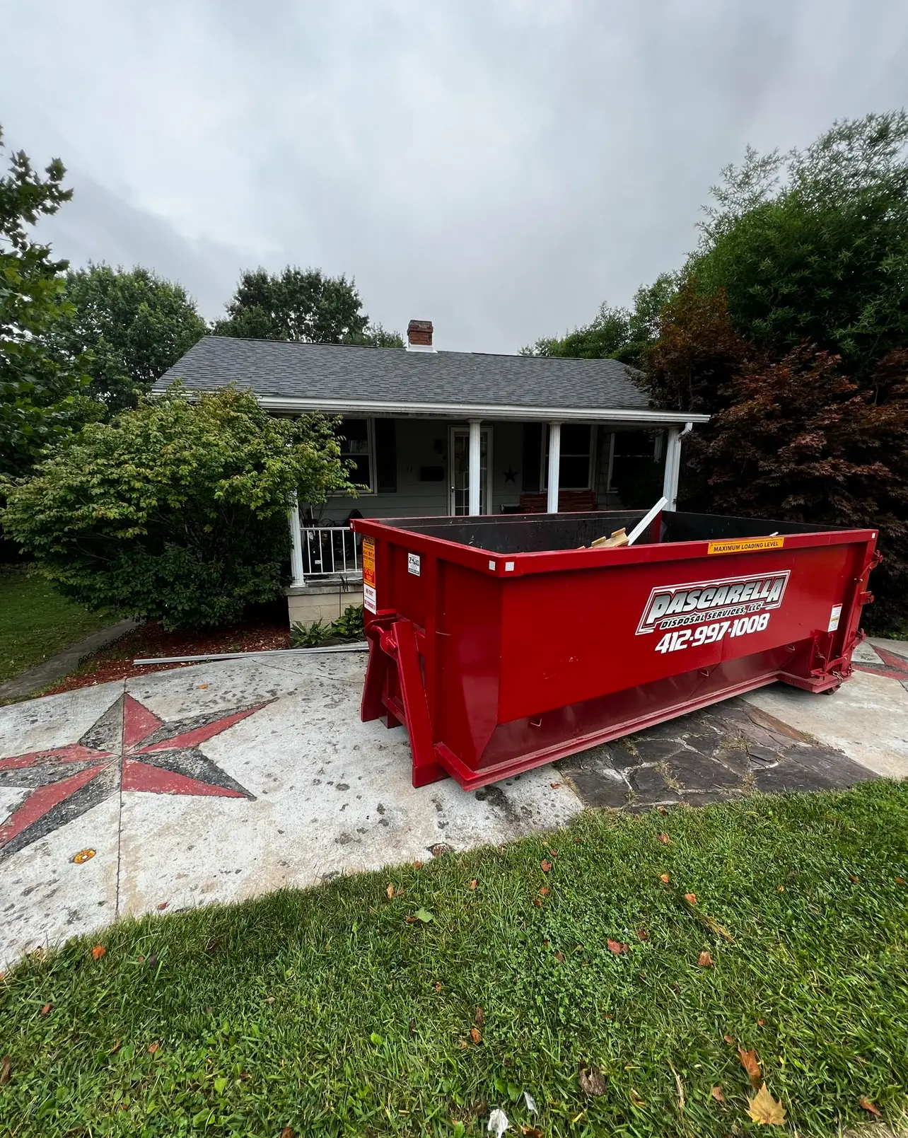 Red Pascarella dumpster staged on protective blocks at a residential home