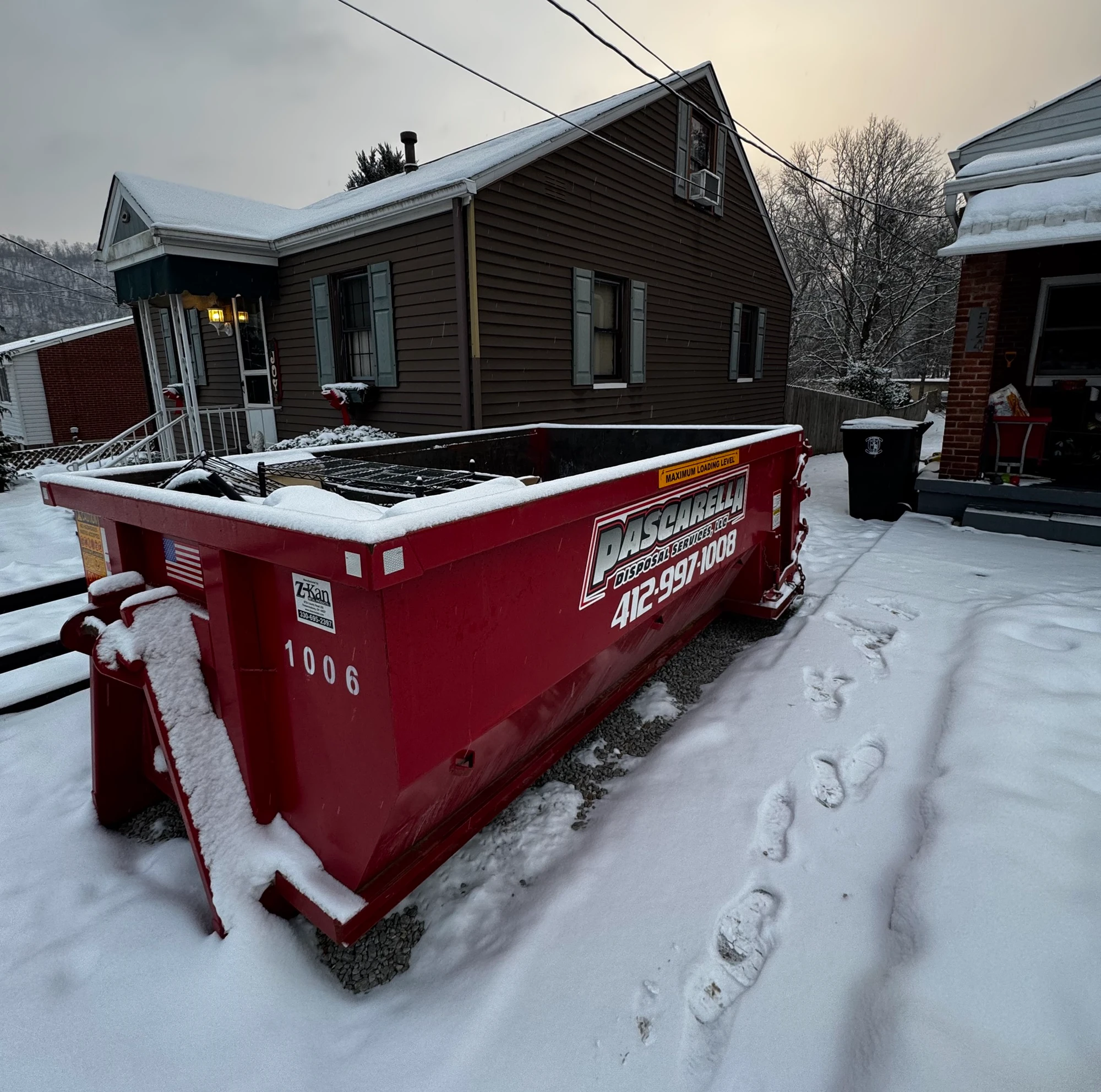 Snow-covered Pascarella dumpster at a winter residential cleanout